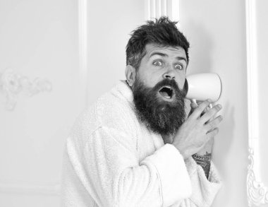 Bornoz şok yüzündeki hipster gizlice konuşma dinle. Gizli ve casus kavramı. Adam sakal ve bıyık kupa duvarının yakınında kullanarak eavesdrops. Adam beyaz iç casusluk, kulak misafiri