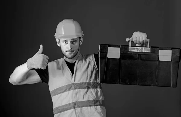 Werknemer, hersteller, reparateur, bouwer op vertrouwen gezicht draagt toolbox op schouder. Reparatie overleg concept. Man in de helm, helm houdt toolbox en toont duim omhoog gebaar, blauwe achtergrond — Stockfoto