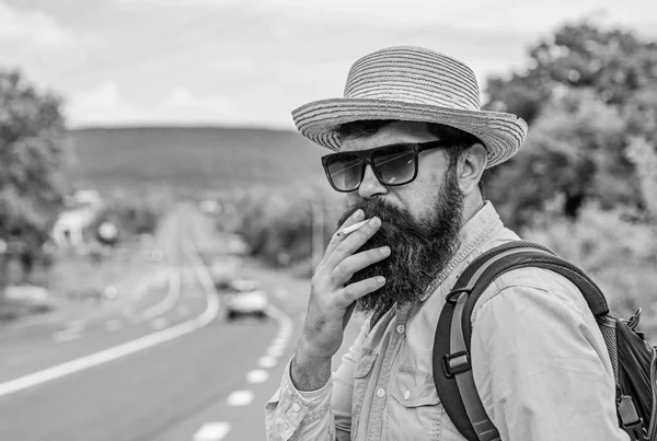 Old habit. Man with beard and mustache in straw hat smoking cigarette, road background defocused. Traveler stylish hipster take brake with cigarette. Smoking cigarette before long journey — Stock Photo, Image
