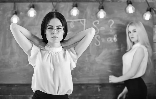 Conceito de alunos e estagiários. Mulheres atraentes preparando-se para a aula. Menina parece atraente enquanto senhora escrevendo no fundo quadro, desfocado. Estudante, professor de óculos em sala de aula — Fotografia de Stock