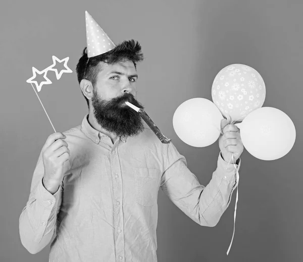 Entertainer with colorful baloons at kids party, international childrens day. Bearded artist with party wistle and paper star shaped glasses wearing birthday cap. Bearded man on blue background