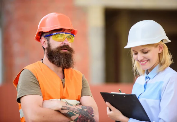 Safety inspector concept. Woman inspector and bearded brutal builder discuss construction progress. Construction project inspecting. Construction site safety inspection. Discuss progress project