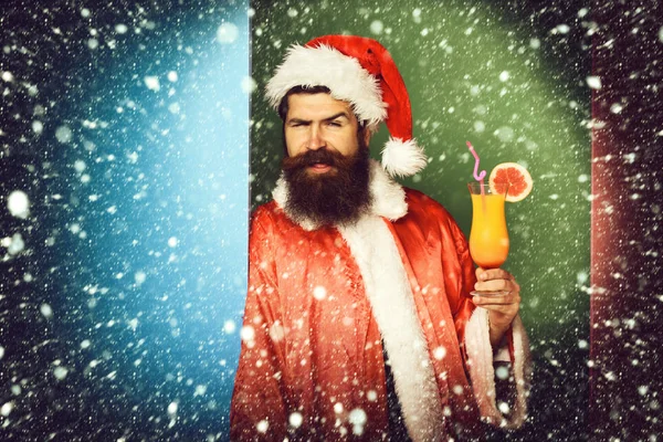 Yakışıklı sakallı Noel Baba adam ile uzun sakallı Noel veya xmas kazak ve renkli stüdyo arka plan, kopya spac yeni yıl şapkası Alkolsüz kokteyl bardak tutan komik yüz — Stok fotoğraf