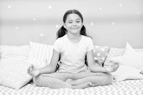 Yatağına git önce meditasyon. Kız çocuk yatak yatak odasında oturmak. Çocuk yatmaya hazırlanın. Keyifli zaman için akşam meditasyon. Rahatlatıcı ve yatak odasında meditasyon kız çocuk uzun saçlı şirin pijama — Stok fotoğraf