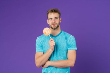 Lolipop eğlencesi. Adam kocaman renkli lolipop yiyor. Tüylü adam lolipopu seviyor. Yemek konseptini aldatmak. Şeker sağlığa zararlıdır. Adamın elinde lolipop şeker menekşesi var. Çocukluk tadı