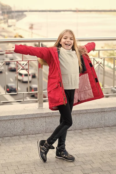 Dítě v červeném kabátě stojí s otevřenými kartami na mostě — Stock fotografie