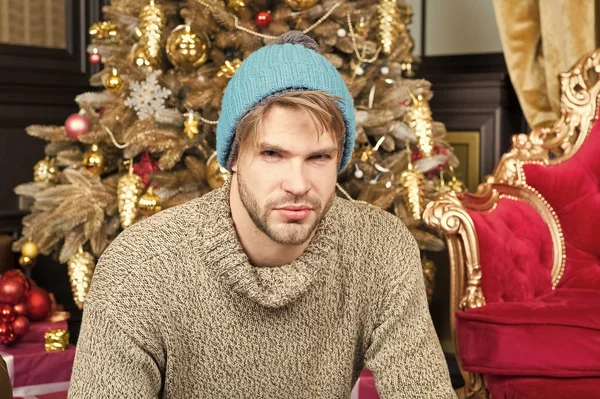 Macho σε ζεστό καπέλο, κάθονται πουλόβερ στο χριστουγεννιάτικο δέντρο — Φωτογραφία Αρχείου