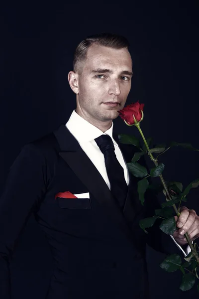 Homem de negócios com flor de rosa vermelha no fundo preto — Fotografia de Stock