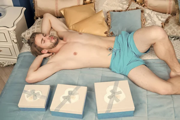 Mann in blauer Unterwäsche schläft auf Bett mit Geschenkboxen — Stockfoto