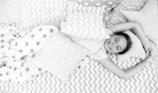 愉快的觉醒。女孩微笑快乐的孩子躺在床上与明星图案枕头和可爱的格子在她的卧室。儿童床上用品。现代时尚的床上用品。女孩早上醒来 — 图库照片