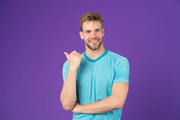 Mira ahí. Concepto masculinidad. Hombre con fuertes brazos musculares. ¿Tener cuerpo muscular te hace más seguro. Hombre musculoso guapo sin afeitar chico en violeta fondo apuntando dedo copia espacio — Foto de Stock