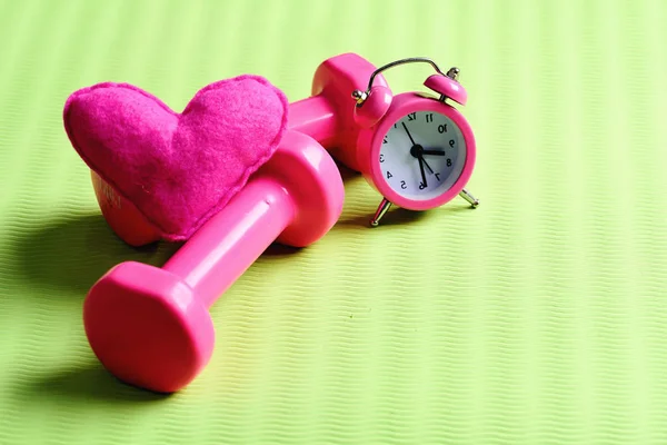Hantlar i rosa färg bredvid väckarklocka och hjärta — Stockfoto