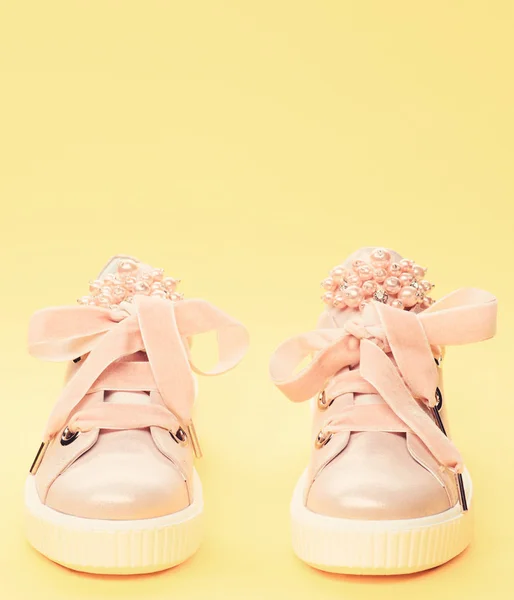 Footwear for girls or women decorated with pearl beads. Comfortable footwear concept. Pair of pale pink female sneakers with velvet ribbons. Cute shoes on yellow background — Stock Photo, Image