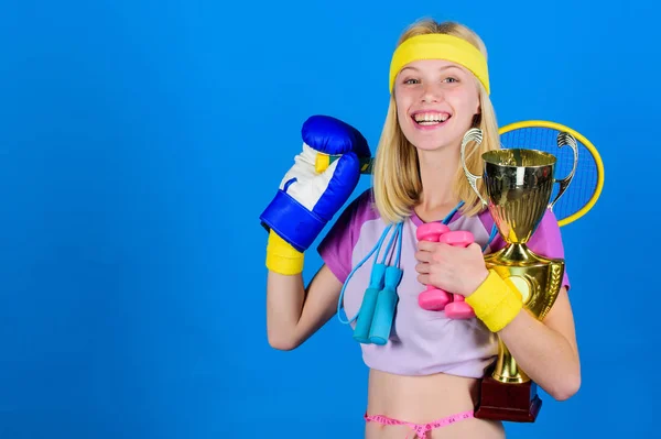 Sport shop assortment. Girl successful modern woman hold golden goblet of sport champion and equipment blue background. Sport for every day. How to find time for everything. Sport equipment store