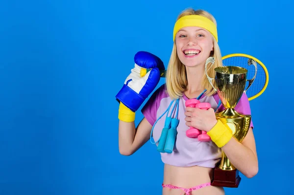 Sport shop sortiment. Flicka framgångsrika moderna kvinna håll gyllene bägare av sport mästare och utrustning blå bakgrund. Idrott för varje dag. Hur att hitta tid för allt. Sport utrustning store — Stockfoto