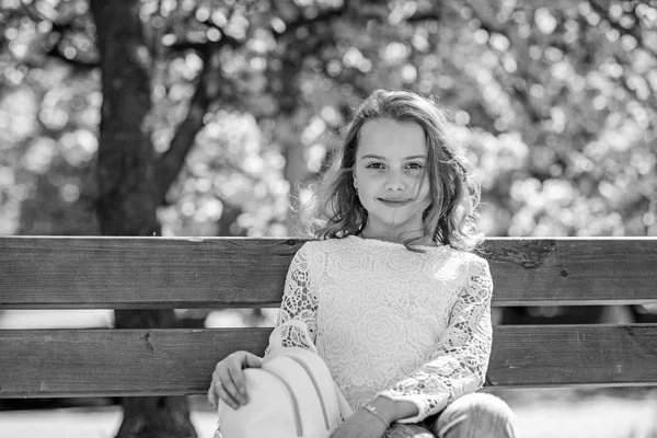 Girl on smiling face sits on bench, sakura tree on background, defocused. Spring walks concept. Cute child with backpack enjoy sunny spring day. Girl relaxing while walk in park near cherry blossom — Stock Photo, Image