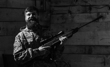 Hunter, silahla acımasız hipster tüfek avcılık için kopya alanı hazırlamak. Avcı kavramı. Sakallı kamuflaj elbiseler, ahşap iç arka plan giyer. Maço gamekeepers evinde mutlu yüz.