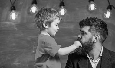 Teacher with beard, father and little son having fun in classroom, chalkboard on background. Dad with beard spend time with son. Child cheerful play with beard of teacher. Fatherhood concept clipart