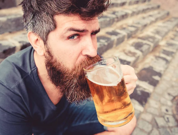 Um tipo a descansar com cerveja gelada. Hipster no rosto calmo bebendo cerveja ao ar livre. Conceito de cerveja. Homem com barba e bigode segura vidro com cerveja enquanto se senta em escadas de pedra — Fotografia de Stock