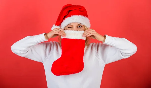 サンタ帽子の女は、クリスマス ギフト赤背景を保持します。少女の陽気な顔は、クリスマスの靴下ギフトを得た。伝統的な冬の休日。クリスマスのストッキングのコンセプトです。クリスマスの靴下の内容を確認します。 — ストック写真