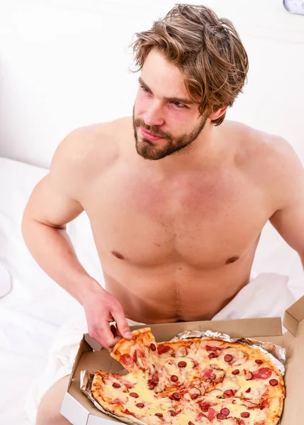 Portrait of lazy muscular man eating pizza while laying on a bed at home. Cropped image of shirtless sexy man with pizza on bed. Break diet concept. — Stock Photo, Image