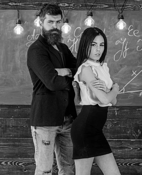 Man met baard en sexy meisje leraar staan in de klas, schoolbord op achtergrond. Partners concept. Lady en hipster samen te werken op school. Leraar en strikte schoolmeester kijken vol vertrouwen — Stockfoto