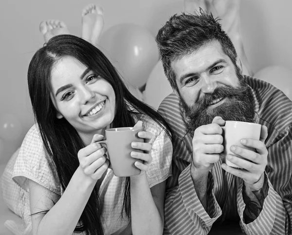 Pareja enamorada bebe café en la cama. Pareja relajarse en la mañana con café. Concepto de tradición familiar. Hombre y mujer con ropa de hogar, pijama. Hombre y mujer en rostros sonrientes, fondo rosa — Foto de Stock