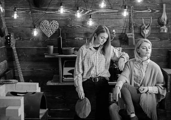 Amigos o hermanas pasan una agradable velada en la casa de guardabosques, fondo interior. Concepto de vacaciones en bosques. Las chicas en caras tranquilas disfrutan de un ambiente cálido mientras descansan. Las niñas disfrutan vacaciones — Foto de Stock