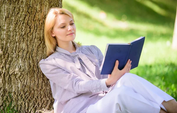 Жіноче самовдосконалення. Дівчина нахиляється на дерево, поки відпочиває в парку сидить трава. Книга самовдосконалення. Концепція самовдосконалення та освіти. Ділова леді знаходить хвилину, щоб читати книгу, щоб поліпшити свої знання — стокове фото