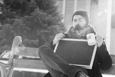 doğal zemin, kopya spac üzerine karlı kış gününde esneme adam, sakal ve bıyık beyaz frost ile kaplı sakallı hippi boş kara tahta veya chalkboard ve Kupası ile ahşap Bank oturur