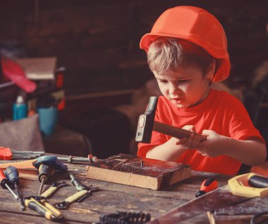 Kask Oluşturucu veya repairer, onarımı veya handcrafting olarak oynayan sevimli çocuk. Meşgul yüz oyunlarında evde atölye üzerinde yürümeye başlayan çocuk. Kavram handcrafting. Çocuk Çocuk ahşap Pano çivi çekiç