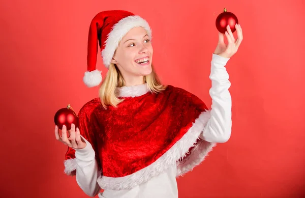 Menina feliz desgaste santa traje comemorar natal segurar bola decoração fundo vermelho. Ano de Natal da época favorita. Feliz Natal e feliz ano novo. Conceito de preparação de Natal. Vamos divertir-nos — Fotografia de Stock