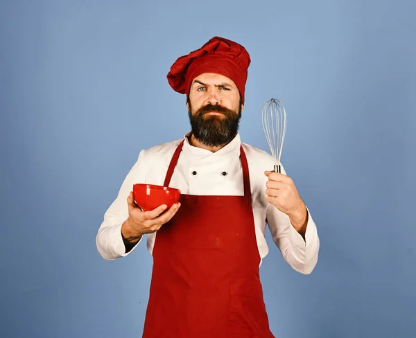 Cook with confused face in burgundy uniform uses kitchenware
