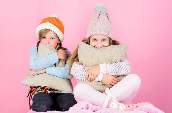 Warm up your winter wear with cute and cozy accessories. Siblings wear winter warm hats sit on pink background. Children boy and girl warm up with pillows and hats. Stay warm and comfortable