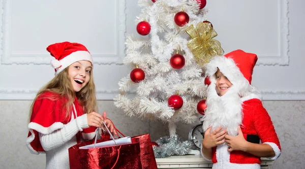 Razón por la que los niños aman la Navidad. Los niños celebran la Navidad con regalos. Niño niño santa con barba artificial blanca y sombrero rojo dan bolsa a la chica. Papá Noel trae regalo de Navidad. Desempaquetar regalos de Navidad —  Fotos de Stock