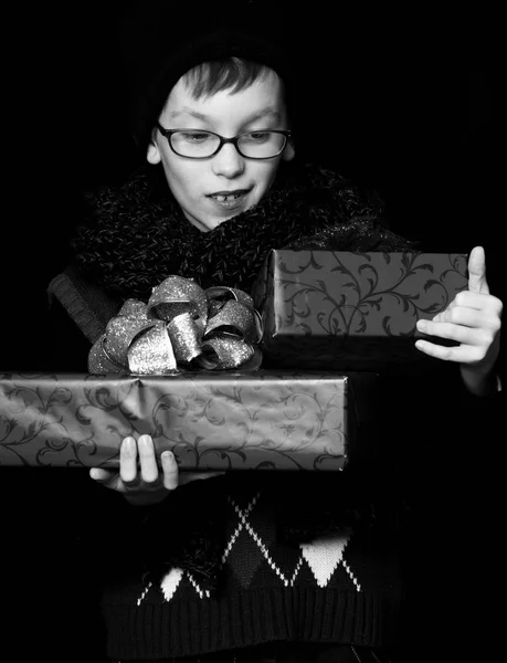 Petit garçon souriant ou mignon nerd kid dans des lunettes, chapeau et foulard tricoté à la mode sur fond noir tient boîtes cadeaux rouges avec bo doré — Photo