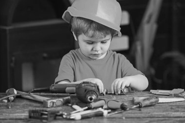 Metal ile oynayan meşgul çocuk cıvata. Tornavida, matkap, çekiç ve küçük ayrıntıları ile masada oturan çalışır