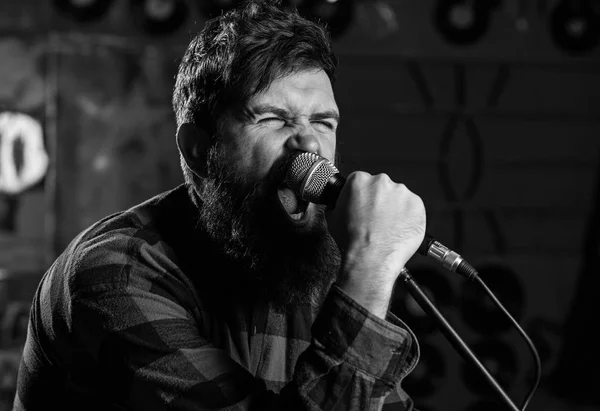 Músico com barba e bigode cantando no karaoke. Conceito de estrela de rock. Homem com rosto tenso segura microfone, canção cantando, fundo do clube de karaoke. O tipo gosta de cantar de forma agressiva — Fotografia de Stock