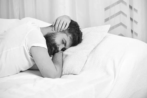 Man in shirt laying on bed covering ears with hands, white curtain on background. Wake up call concept. Macho with beard and mustache refuses to get up. Guy on sleepy tired face keep sleeping