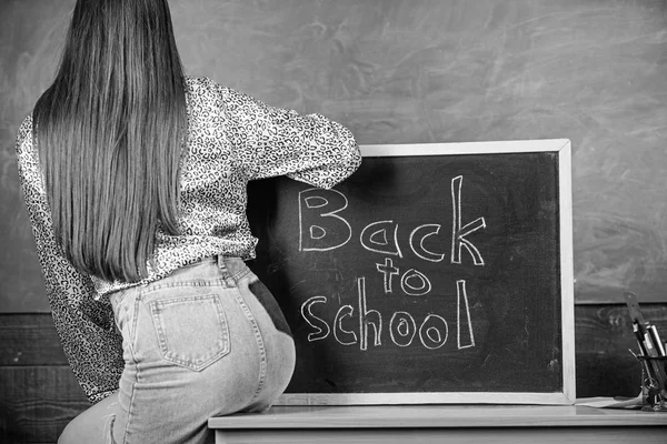 Code vestimentaire scolaire. Jupe en jean fille enfreignant les règles de vêtements scolaires. Étudiant professeur mini jupe sexy fesses assis tableau noir inscription retour à l'école. Étudiant dos et fesses près du tableau — Photo