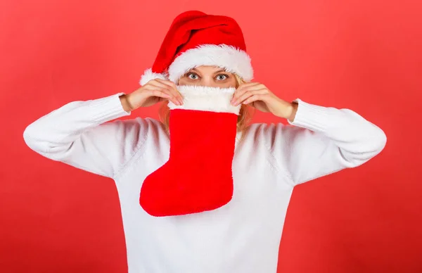 Ellenőrizze a karácsonyi állomány tartalmát. Nő a santa kalap tartja karácsonyi ajándék piros háttér. Lány vidám arc kapott ajándékot a karácsonyi zokni. Hagyományos téli üdülés. Karácsonyi harisnya koncepció — Stock Fotó