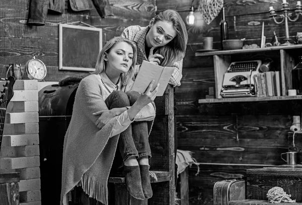 Mamá e hija con mirada concentrada leyendo juntas, concepto de educación en el hogar. Hermosas damas rubias entretenidas por un libro interesante. Hermanas pasar tiempo en casa de madera vieja, interior de estilo retro — Foto de Stock