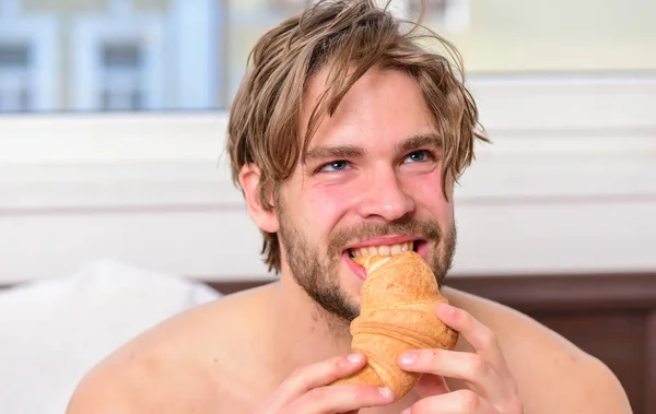 Man eats croissant and drinking coffee. Relaxation and recreation. Handsome man browsing internet in bed. Morning man coffee.