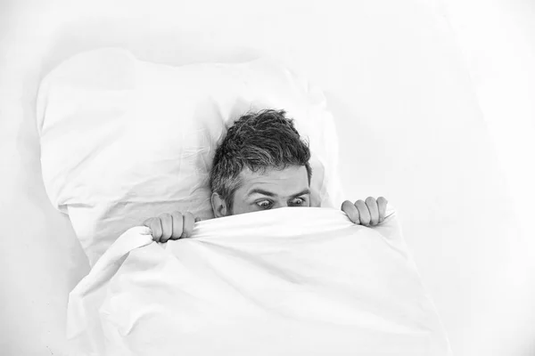 Nightmare concept. Guy hides face under blanket.