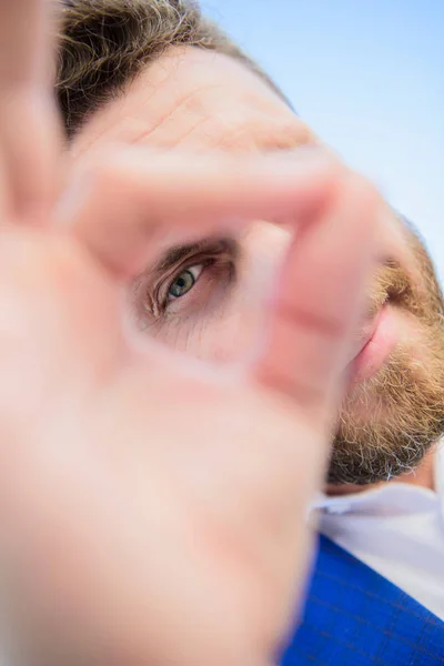 Guy looks suspicious through ok gesture close up. Excellent concept. Spying watching and observing. Man bearded businessman formal suit watching through fingers. I am watching you. Perfect gesture