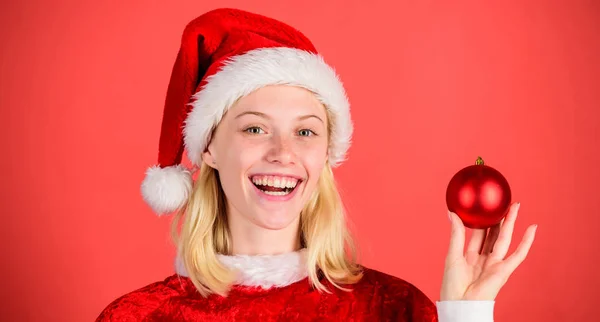 Geniet van de viering gelukkig Nieuwjaar. Kerst voorbereiding concept. Kerstmis fun. Meisje gelukkig slijtage santa kostuum vieren Kerstmis greep bal decor rode achtergrond. Favoriete tijd jaar kerst — Stockfoto