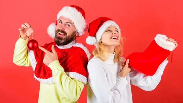 Coppia Natale Babbo Natale costume tenere calzino e palla ornamento. Concetto di festa di Natale. Donna e uomo barbuto in cappello da Babbo Natale in attesa di sfondo rosso Natale. Natale calza tradizione — Foto Stock