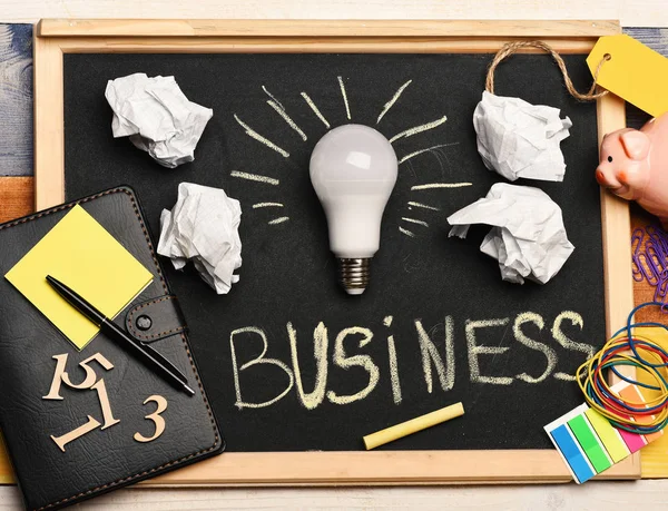 Idea lamp with business accessories on grey chalkboard.
