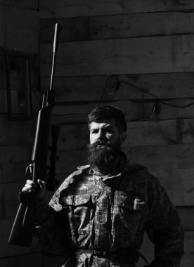 Sakallı kamuflaj elbiseler, ahşap iç arka plan giyer. Maço gamekeepers evinde sıkı yüzünde. Avcı, acımasız hipster silahla avlamaya hazır. Avcı kavramı