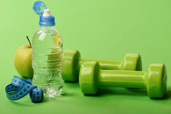 Haltères en couleur verte, bouteille d'eau, ruban à mesurer et fruits — Photo